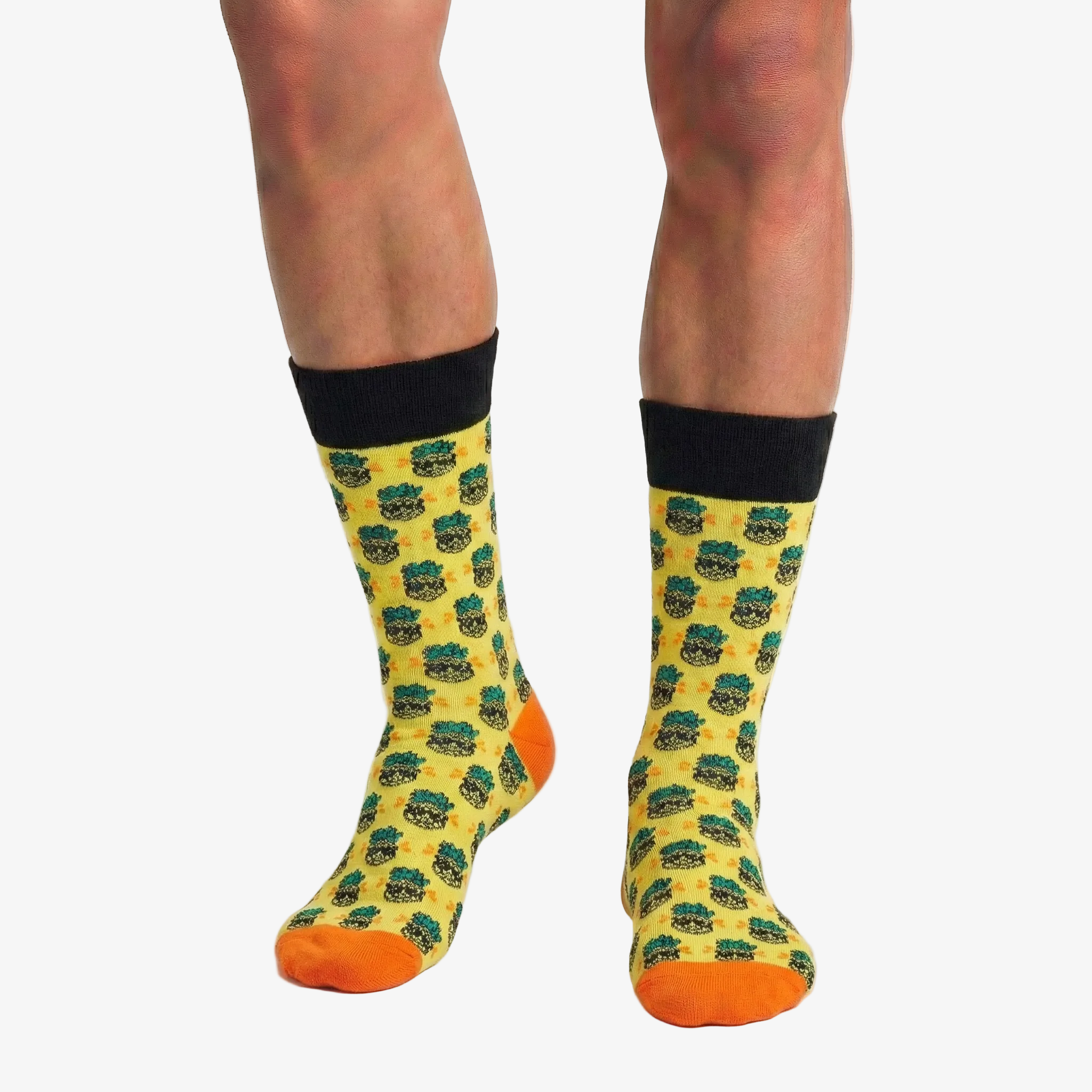 Yellow pineapple socks with black patterns and orange toes worn by a person on a white background